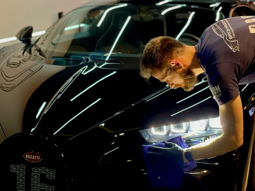 Detailing professional beside a glossy black car for ceramic coating